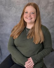 A professional headshot of Keayra Hamby wearing a green long sleeve shirt against a gray background.