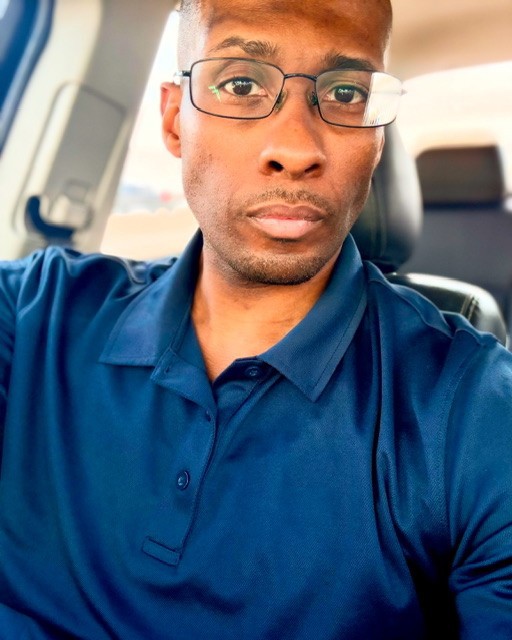 A photo of Christopher Allen Whitney wearing reading glasses and a blue collared shirt.