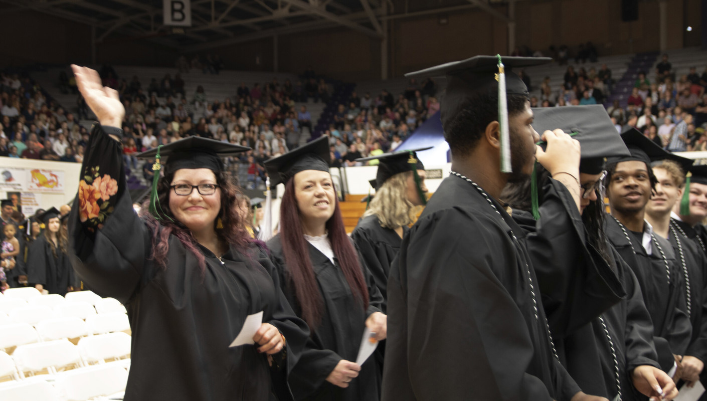 A graduate waving at the camera as she waits for her name to be called
